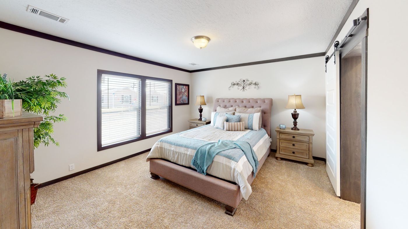 Bedroom with a bed, nightstands, a large window, and beige carpet.