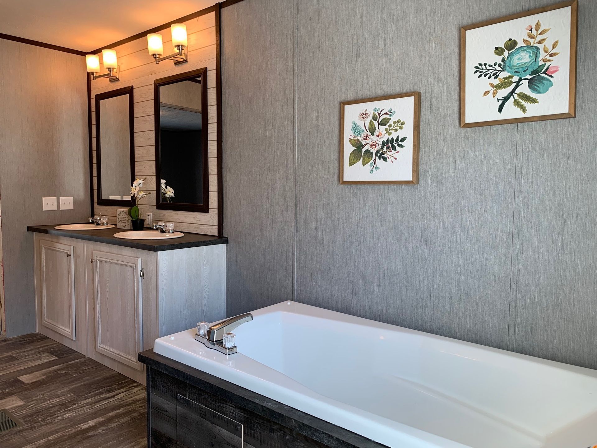 Bathroom with double vanity, framed mirrors, artwork, and a long bathtub.