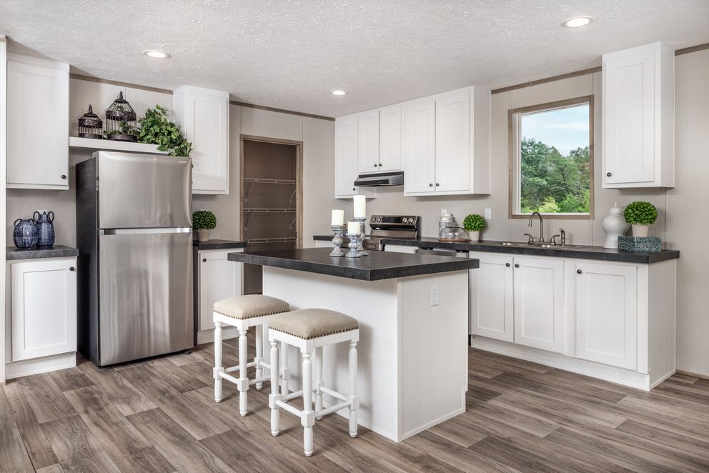 White kitchen with stainless steel appliances, island with stools, and a window overlooking trees.
