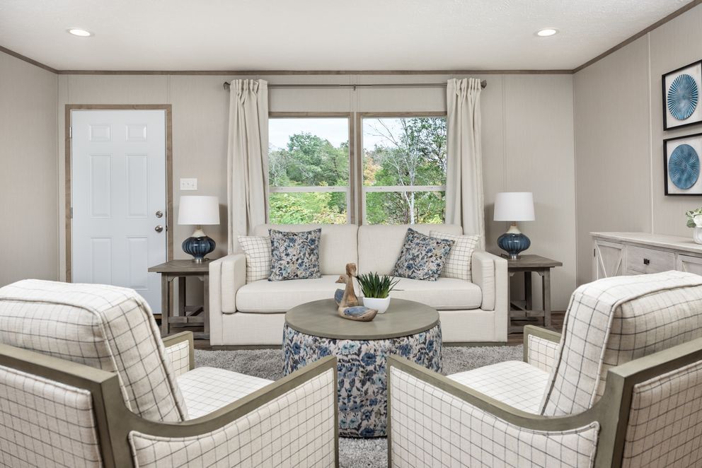 Living room with neutral tones, sofa, two armchairs, side tables, and a central ottoman.