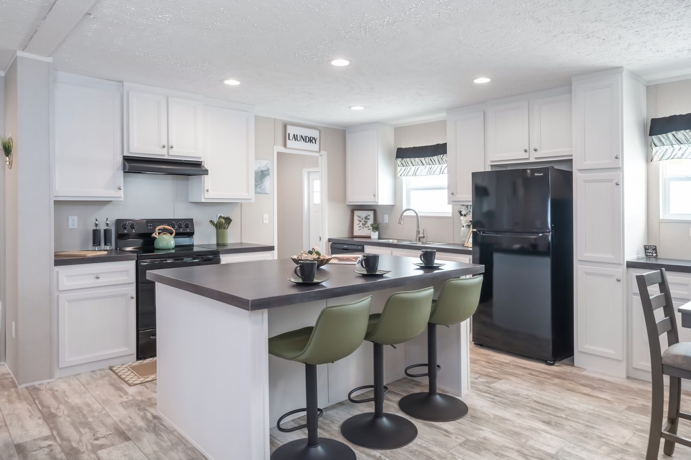 Modern kitchen with white cabinets, black appliances, island with green stools, and gray countertop.