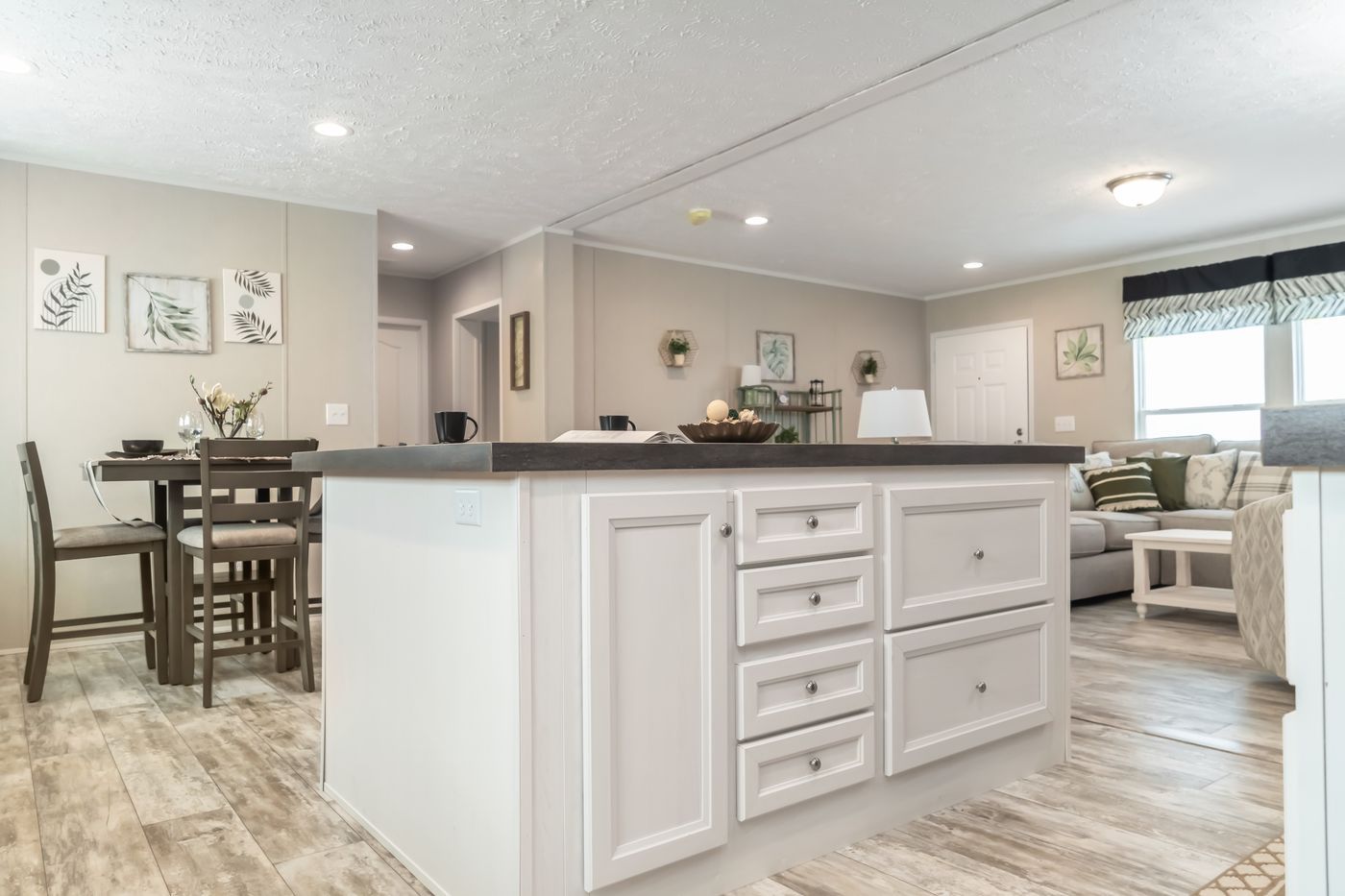 Interior view of a kitchen island with white cabinets, a dining table, and a living room in a modern home.