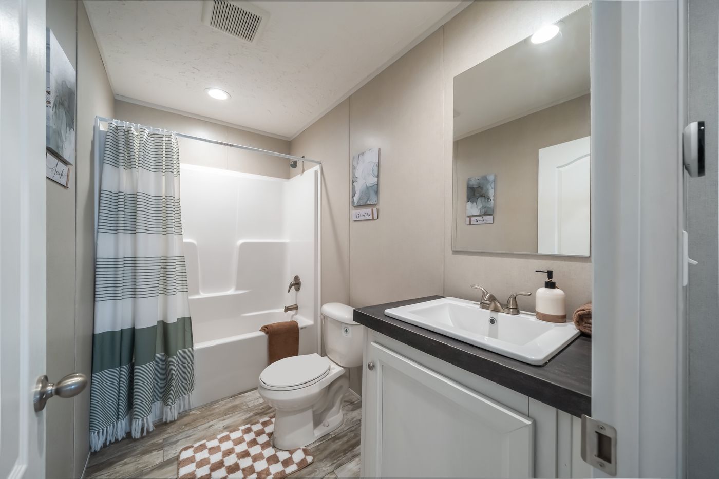 Bathroom with a white tub and toilet, white vanity, neutral walls, striped shower curtain and brown accents.