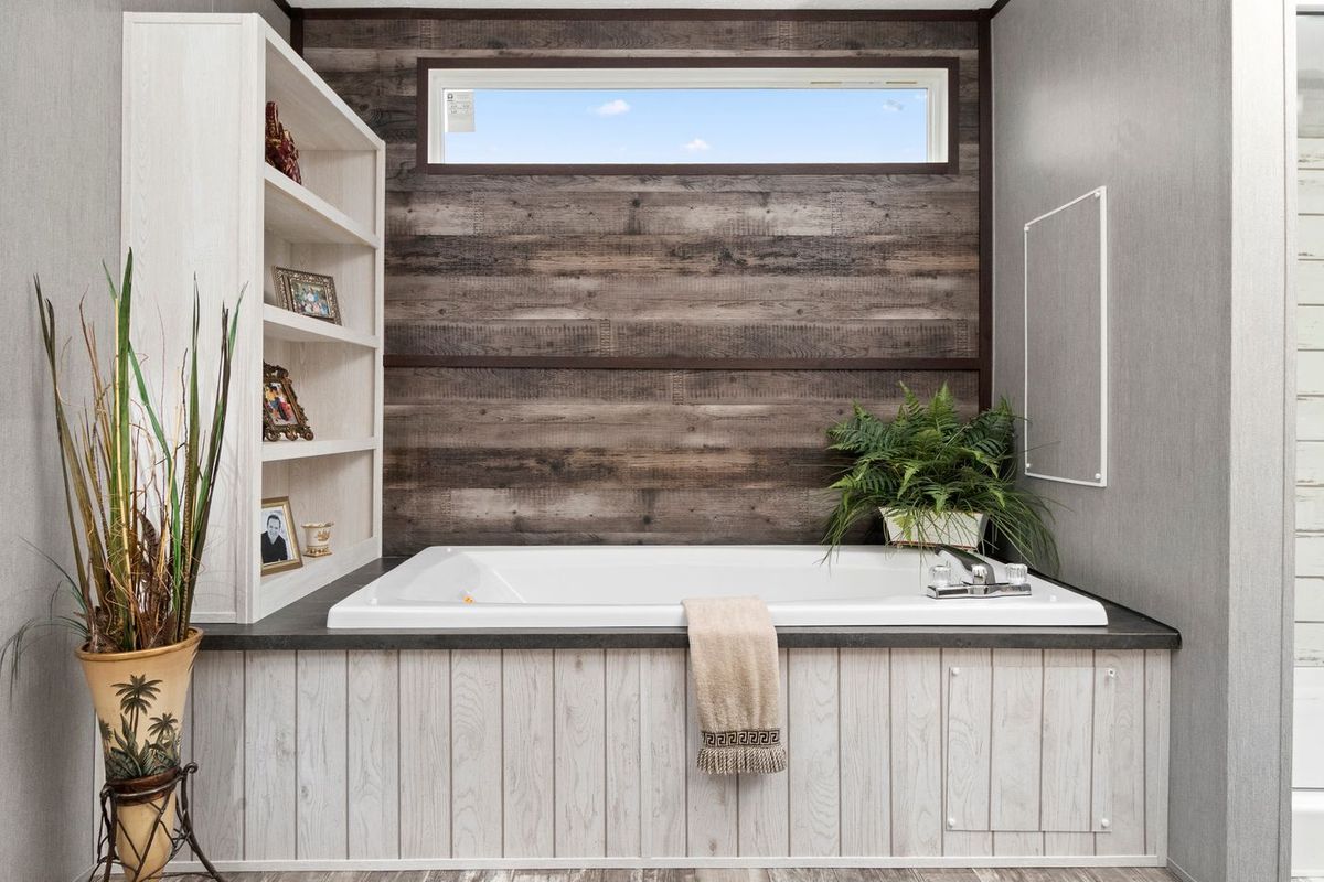 Bathroom with a white bathtub, wood-paneled walls, built-in shelves, and a window.
