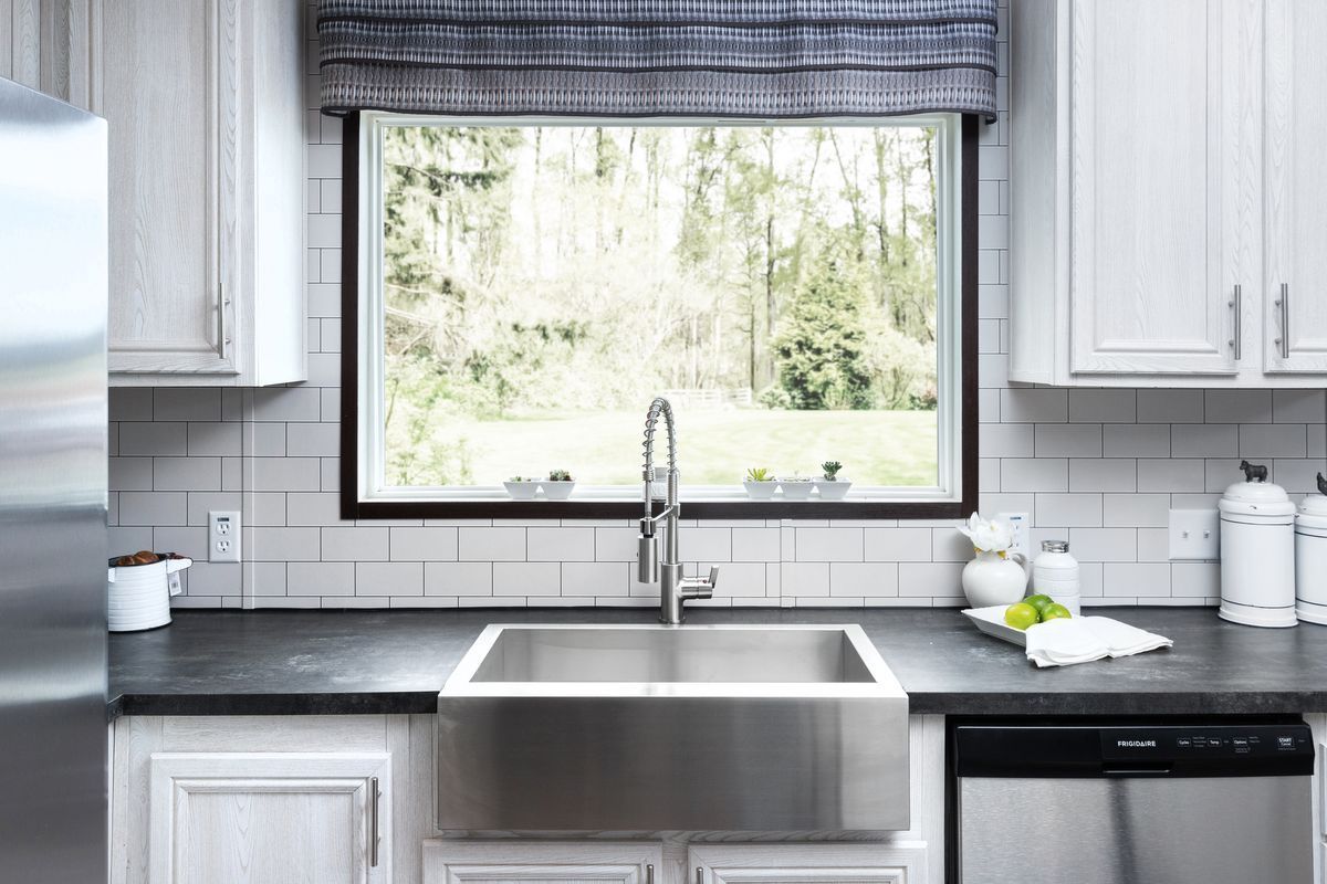 Kitchen with a stainless steel sink in front of a window with a view of trees.