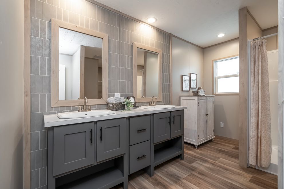 Bathroom with gray tile, double vanity, wood floors, and a window.