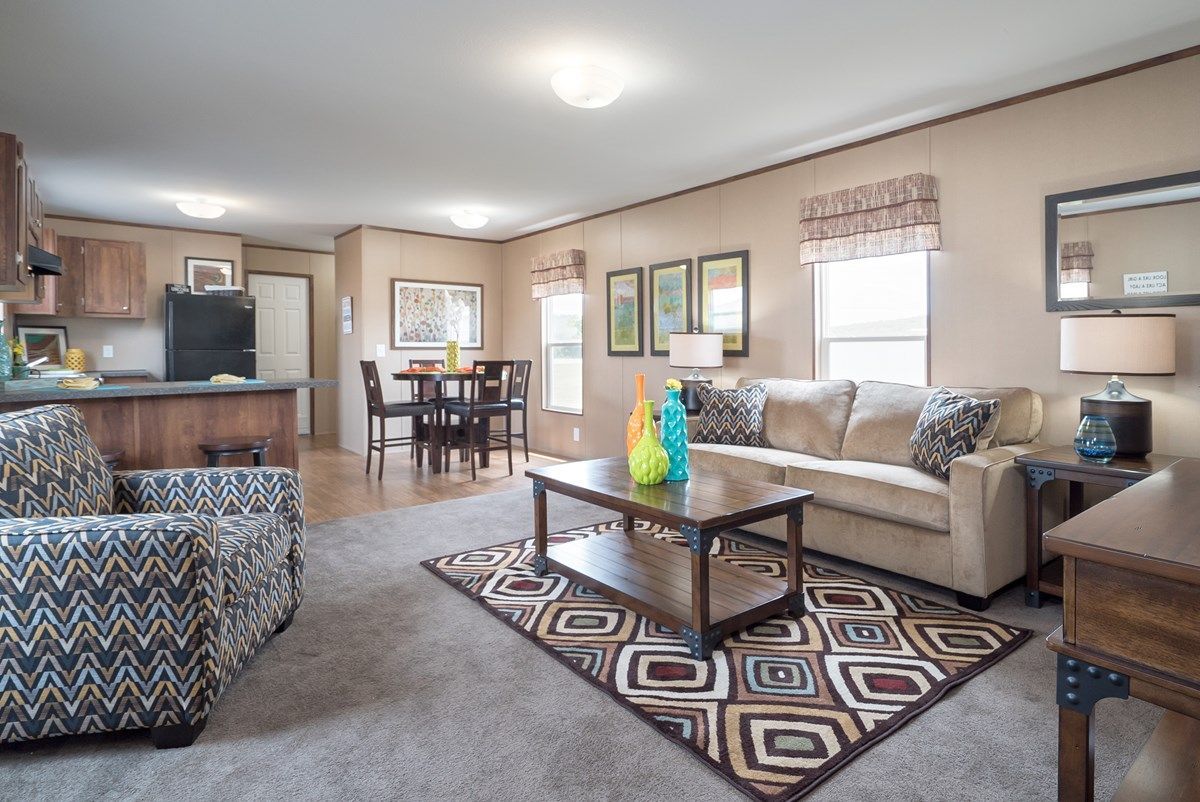 Cozy living room with a patterned rug, sofa, and armchair; the kitchen and dining area are visible.