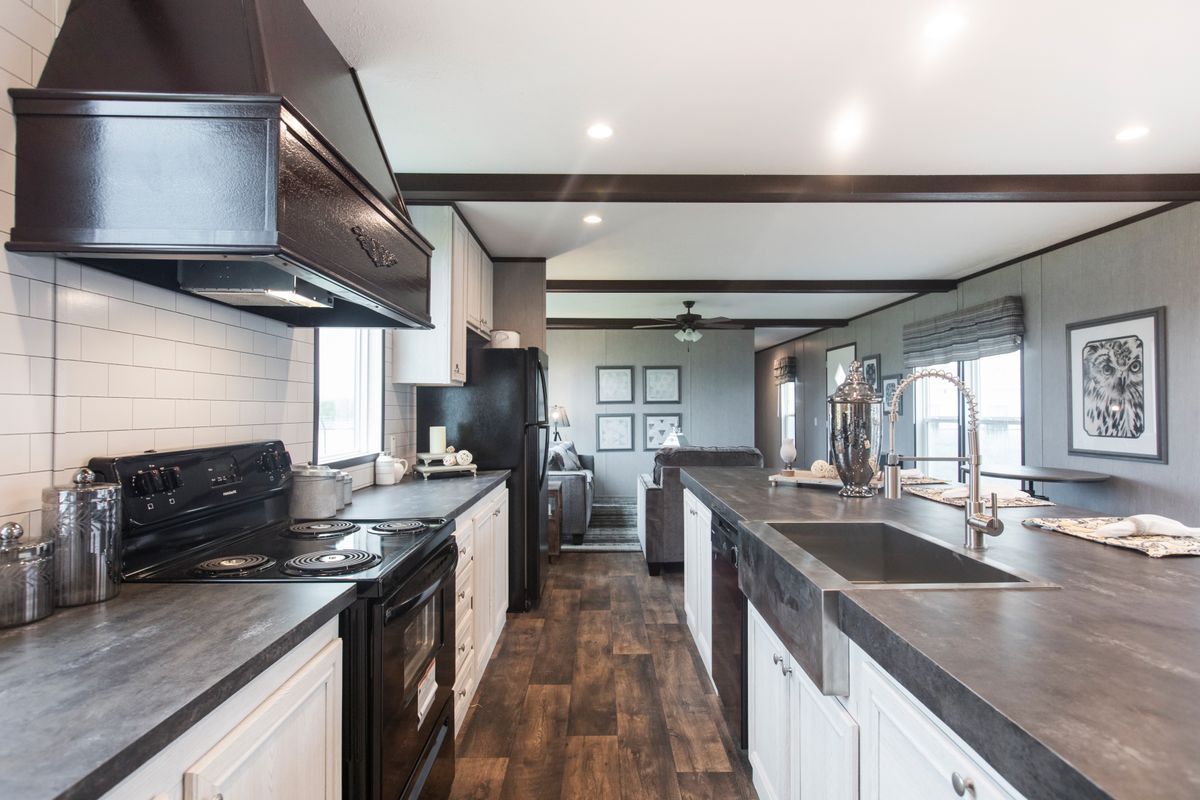 Modern kitchen with white cabinets, black appliances, and dark countertops; brown wood floor.
