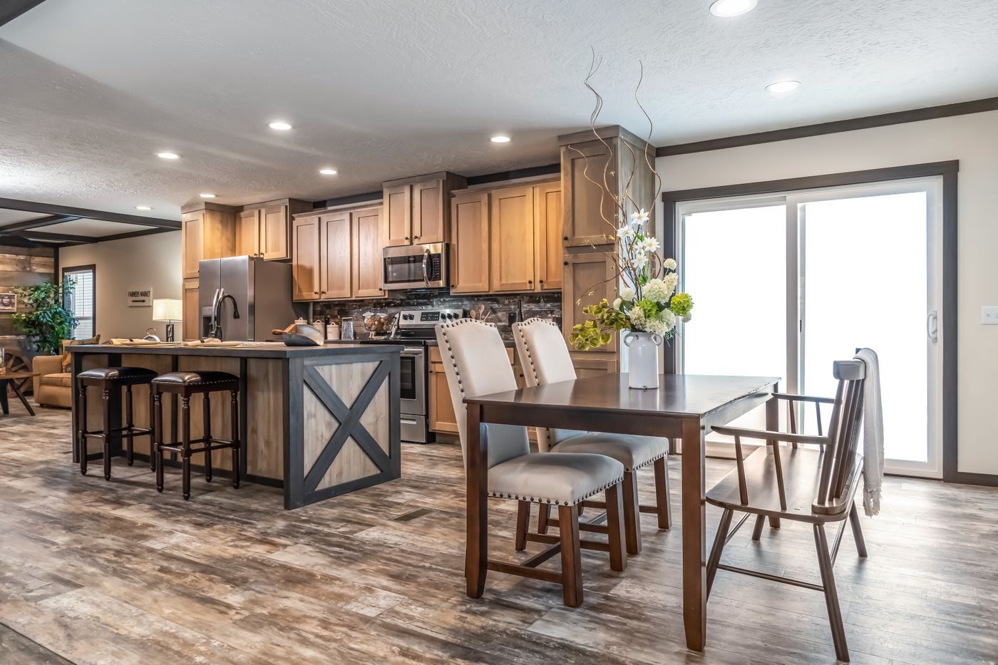 Open kitchen with dining area, wood cabinets, island with stools, dark dining table, sliding glass door.