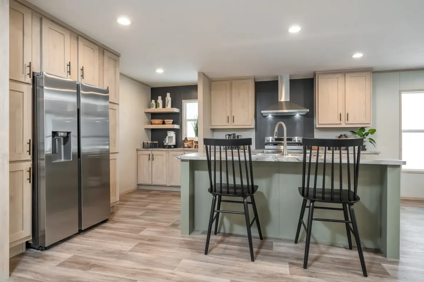 Modern kitchen with a stainless steel fridge, green island, and black chairs.