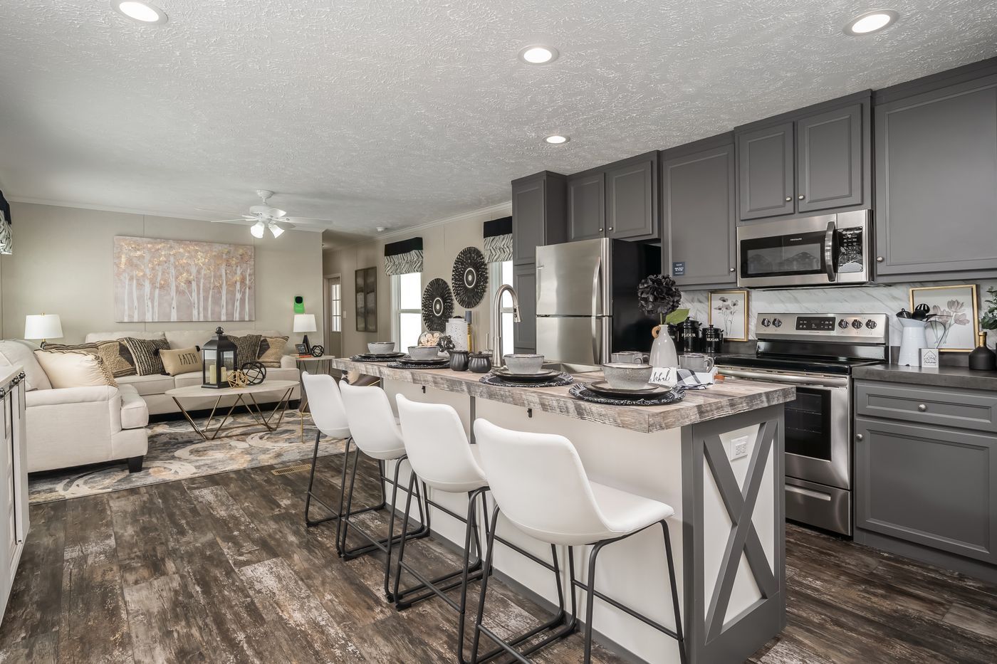 Modern kitchen with island seating, gray cabinets, stainless steel appliances, and living room visible.