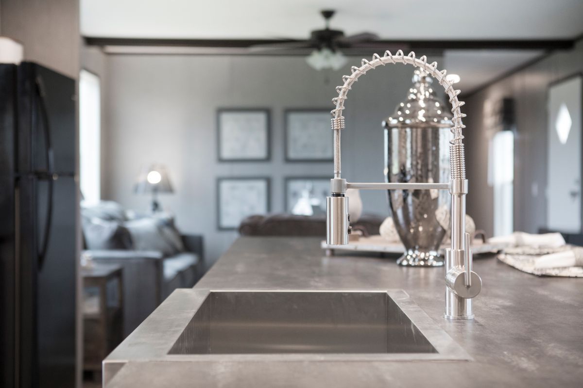 Stainless steel kitchen sink with a pull-down faucet, concrete countertop, blurred living room background.