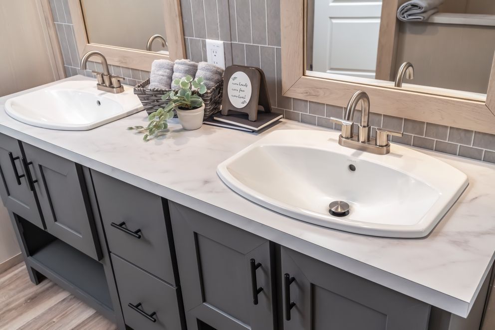 Gray bathroom vanity with two sinks, framed mirrors, and decorative items.