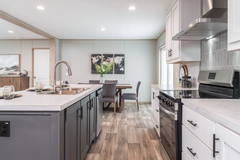 Modern kitchen with island and dining area, gray and white cabinets, stainless steel appliances, wood floor.