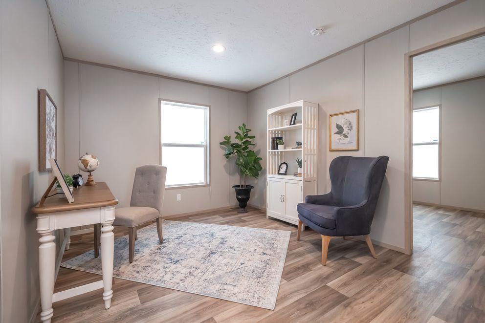 A well-lit home office with a desk, chairs, bookcase, and a rug on wooden floors.