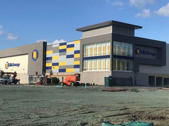 Exterior view of a Life Storage facility under construction. Building is gray with yellow, blue, and white accents; workers and equipment present.