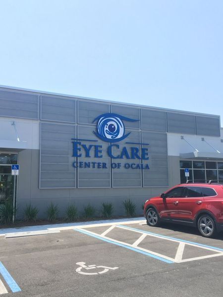 Eye Care Center of Ocala building with blue logo, parked red car, and blue sky.