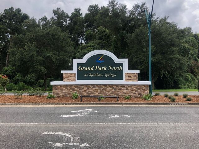 Sign for Grand Park North at Rainbow Springs, with a brick base and green and blue accents, set against trees.