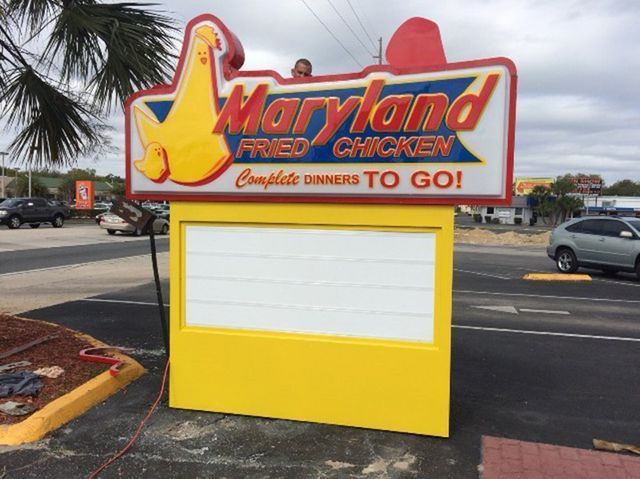 Maryland Fried Chicken sign with yellow and red box for menu, in front of street.
