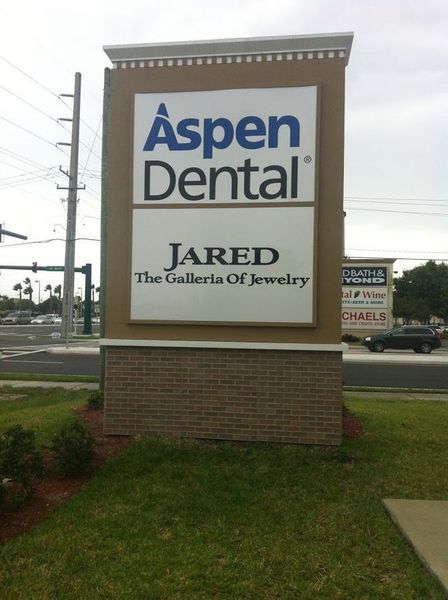 Sign with Aspen Dental and Jared The Galleria Of Jewelry logos. Brick base, beige, blue, and white.