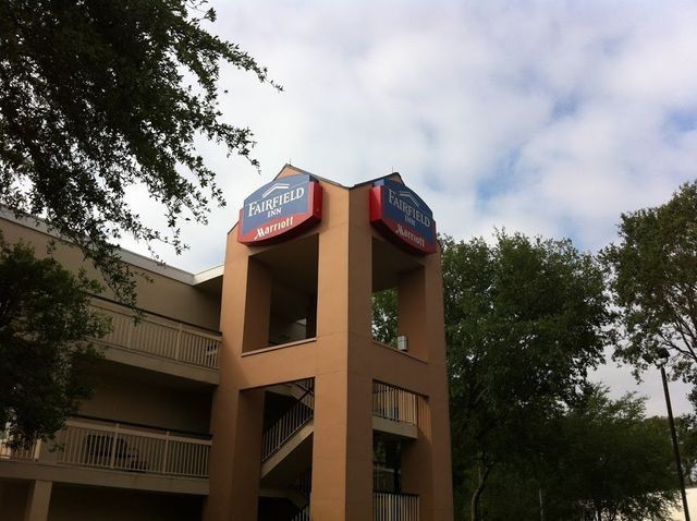 Fairfield Inn hotel sign on a beige building with a staircase, surrounded by trees under a cloudy sky.