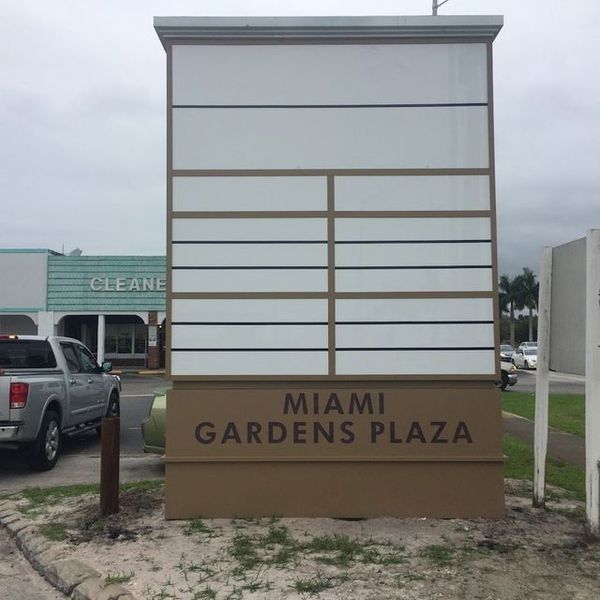 Sign for Miami Gardens Plaza with blank panels for tenant names, in front of a gray sky.
