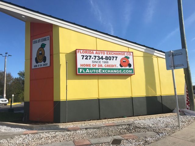 Florida Auto Exchange Co. building with orange, yellow, and green facade; sign with phone number, website, and logo.