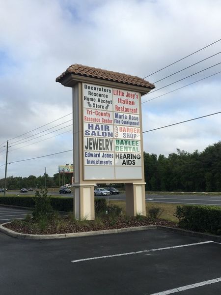 Sign with business names, including a restaurant, hair salon, and jewelry store, on a roadside.