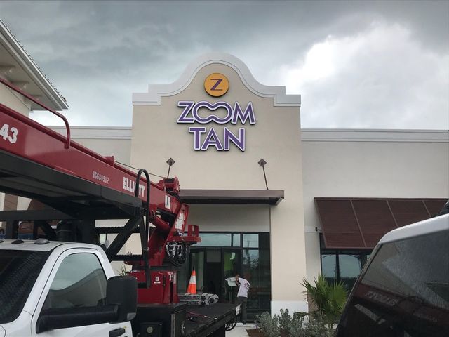 Zoom Tan storefront with sign being worked on, red truck, cloudy day.