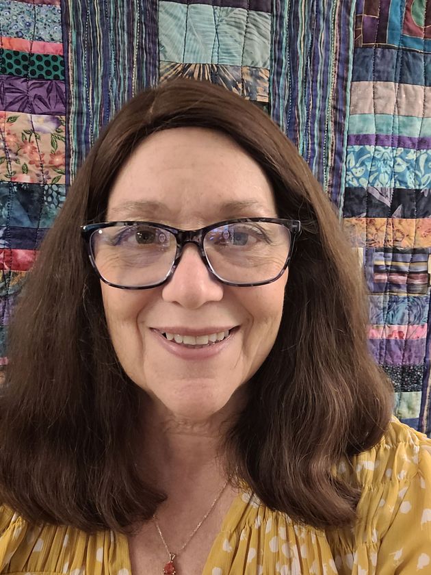 Smiling woman with glasses in front of a colorful quilt backdrop