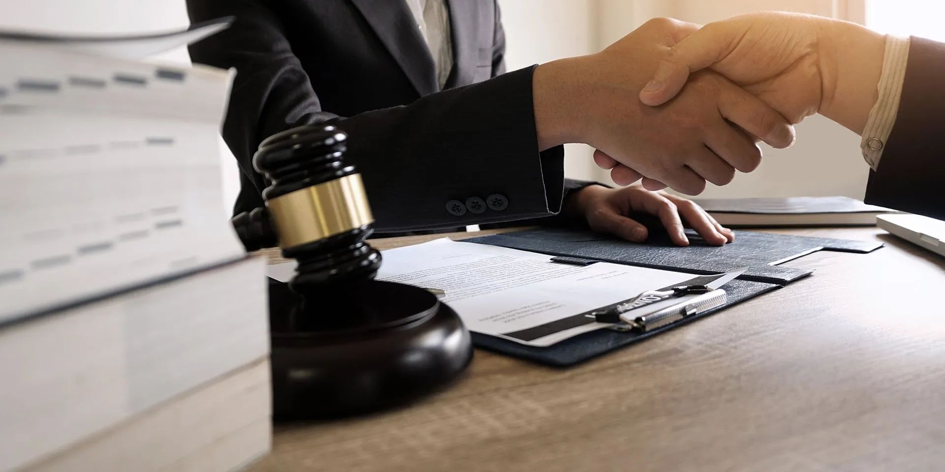 Business handshake beside a judge’s gavel and documents on a desk