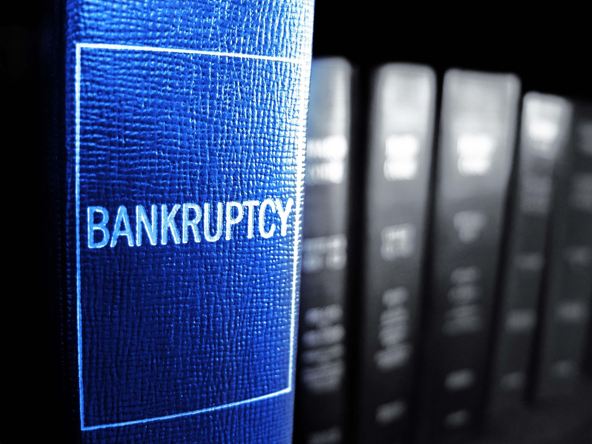 Blue binder labeled BANKRUPTCY on a shelf of blurred black binders