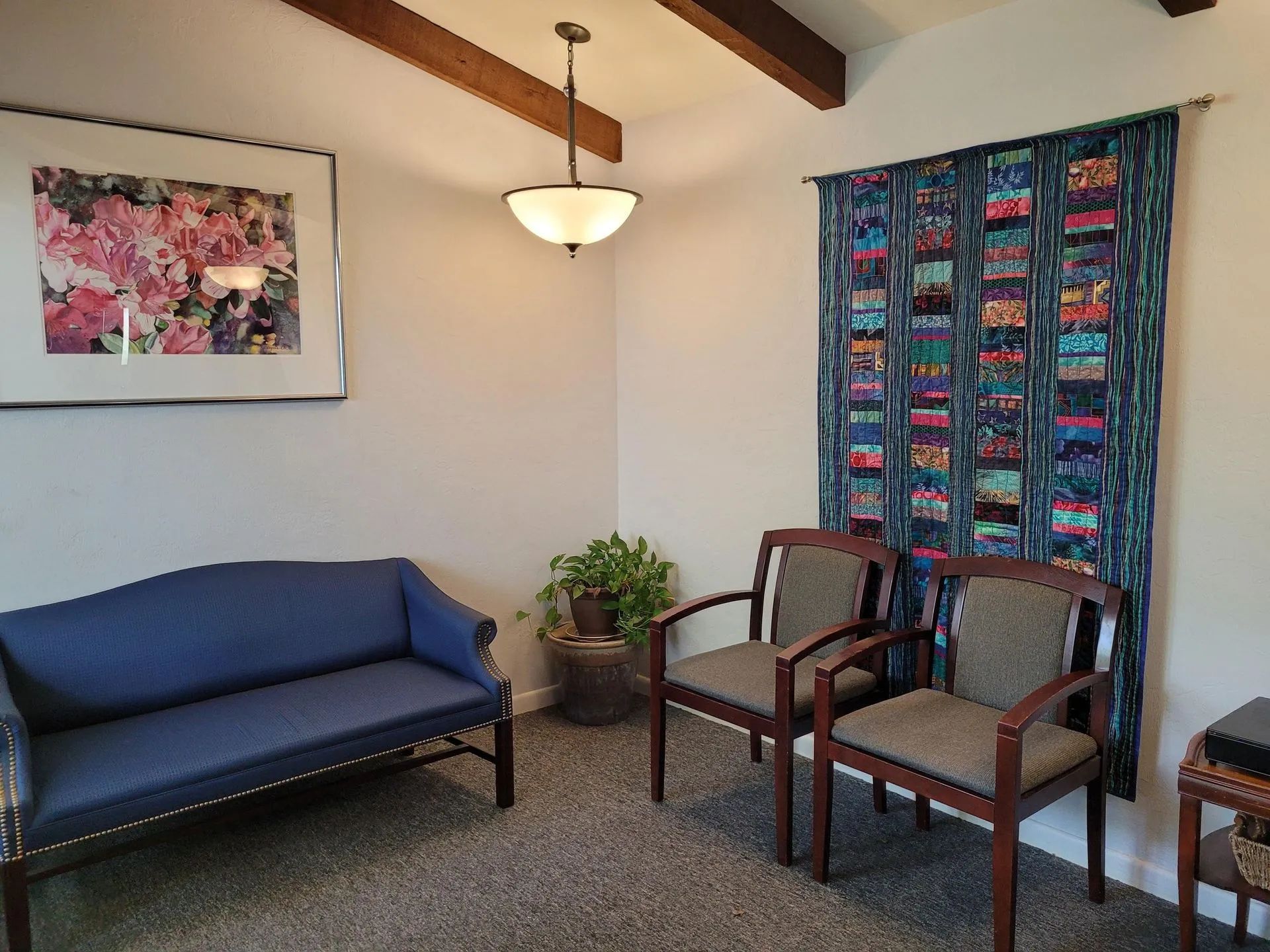 Small living room with blue sofa, two armchairs, colorful curtain, and wall art beneath a hanging light.