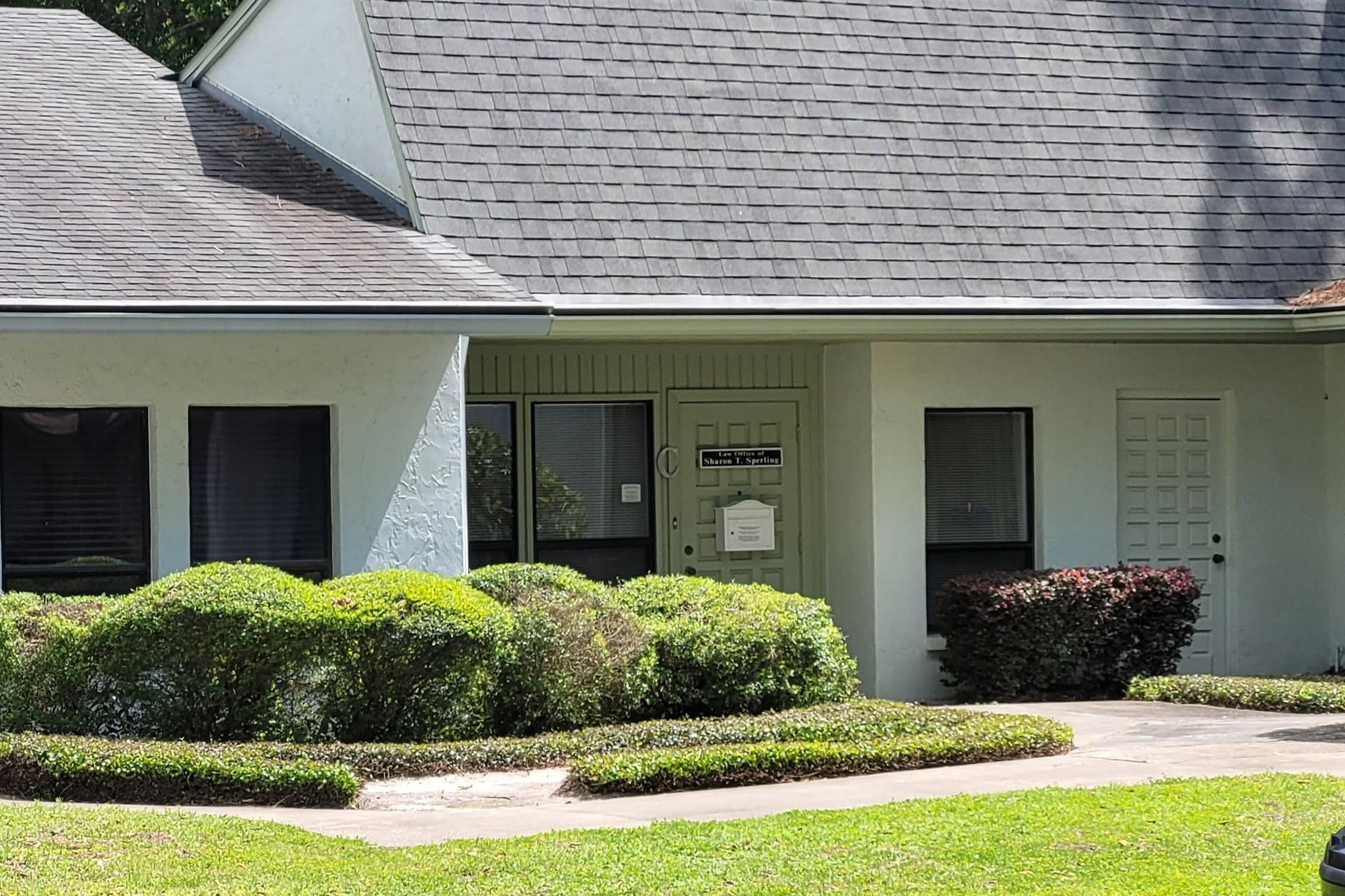Single-story building with a gray roof, green shrubs, and a front entrance with windows and a door
