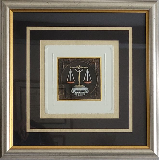Framed artwork with a scales-of-justice symbol centered in layered beige and dark borders