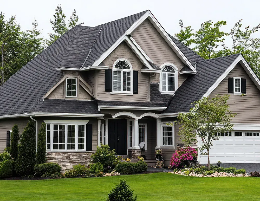 A two-story suburban house with beige siding, a dark roof, white trim, a stone foundation, and a lush green front lawn.