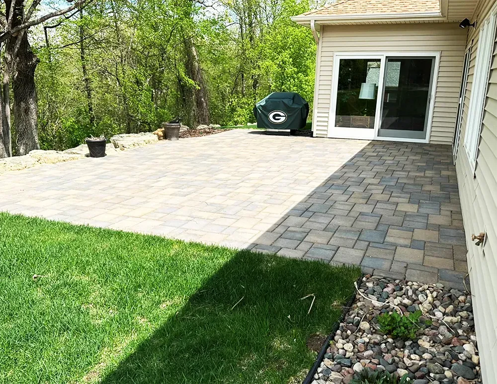 A backyard stone patio featuring a lighter-colored dining area and a darker walkway leading to a house sliding door.