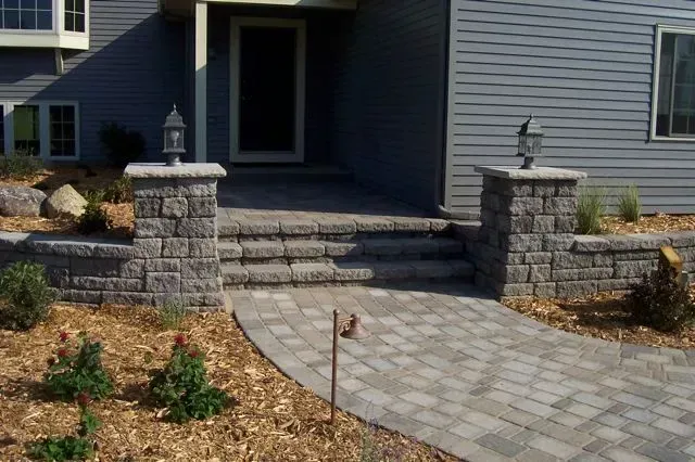 A paved walkway leads to three stone steps and a front entryway with two stone pillars topped by lanterns.