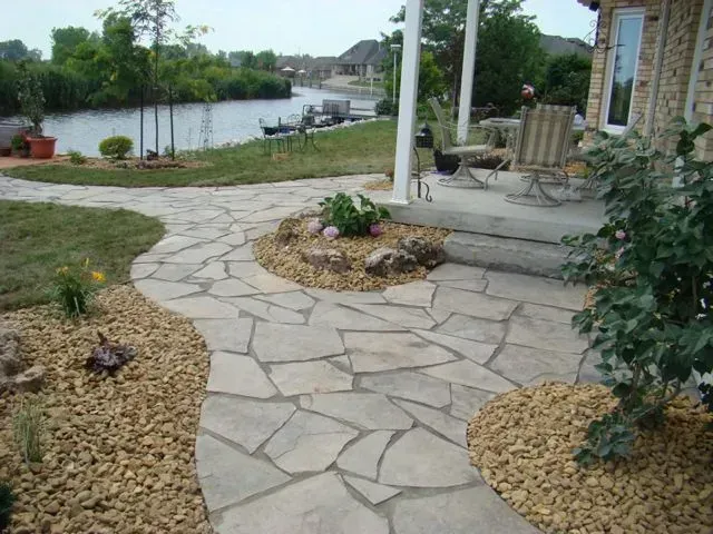 Flagstone path winding through a garden towards a patio overlooking a river.