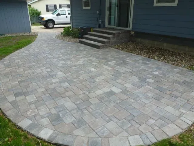 A new, gray-toned paver patio and walkway leading to a set of matching stone steps at a house entrance.
