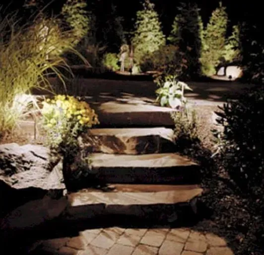 A stone staircase in a landscaped garden at night, illuminated by warm outdoor accent lighting.