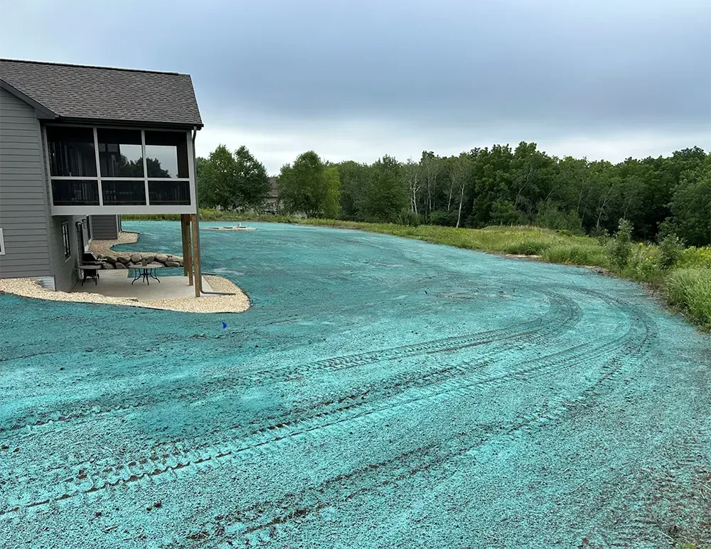 A house with a screened-in porch overlooks a backyard recently covered in green hydroseeded soil and tire tracks.