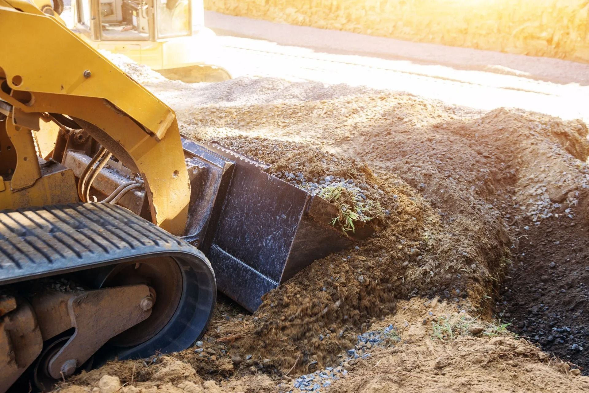 A close-up view of a yellow skid-steer loader pushing a pile of soil and gravel at a construction site.