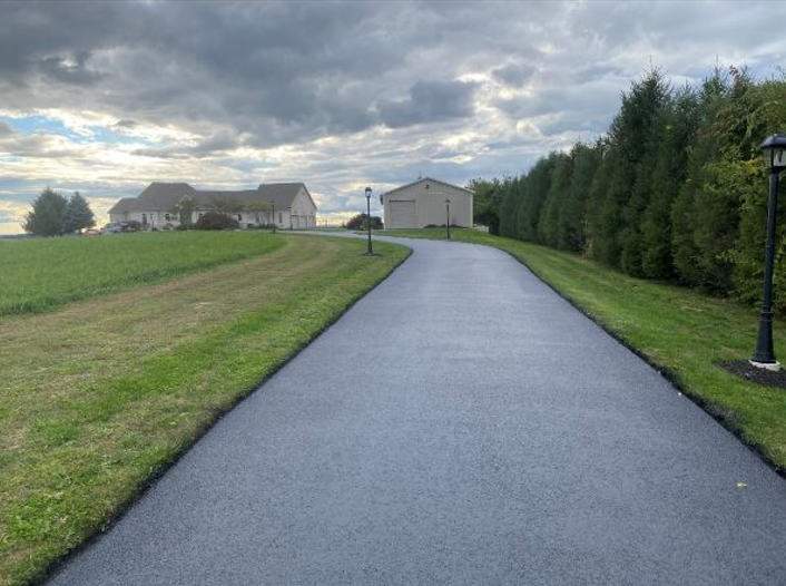 A driveway leading to a house in the middle of a grassy field.