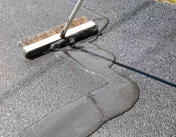 A person is using a broom to spread asphalt on the ground.