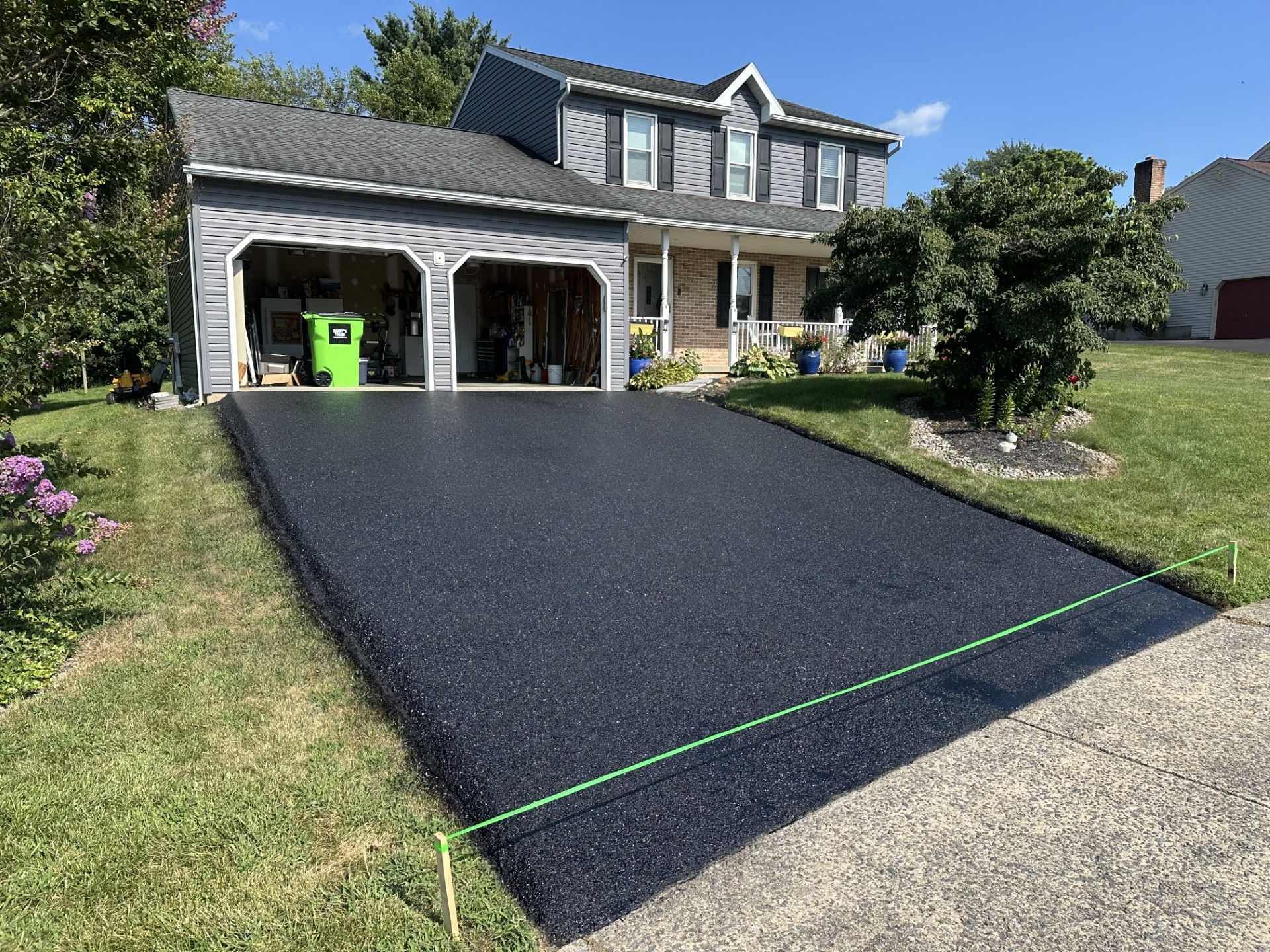 A two-story house with a newly paved, dark asphalt driveway and a green string line marking its edge.