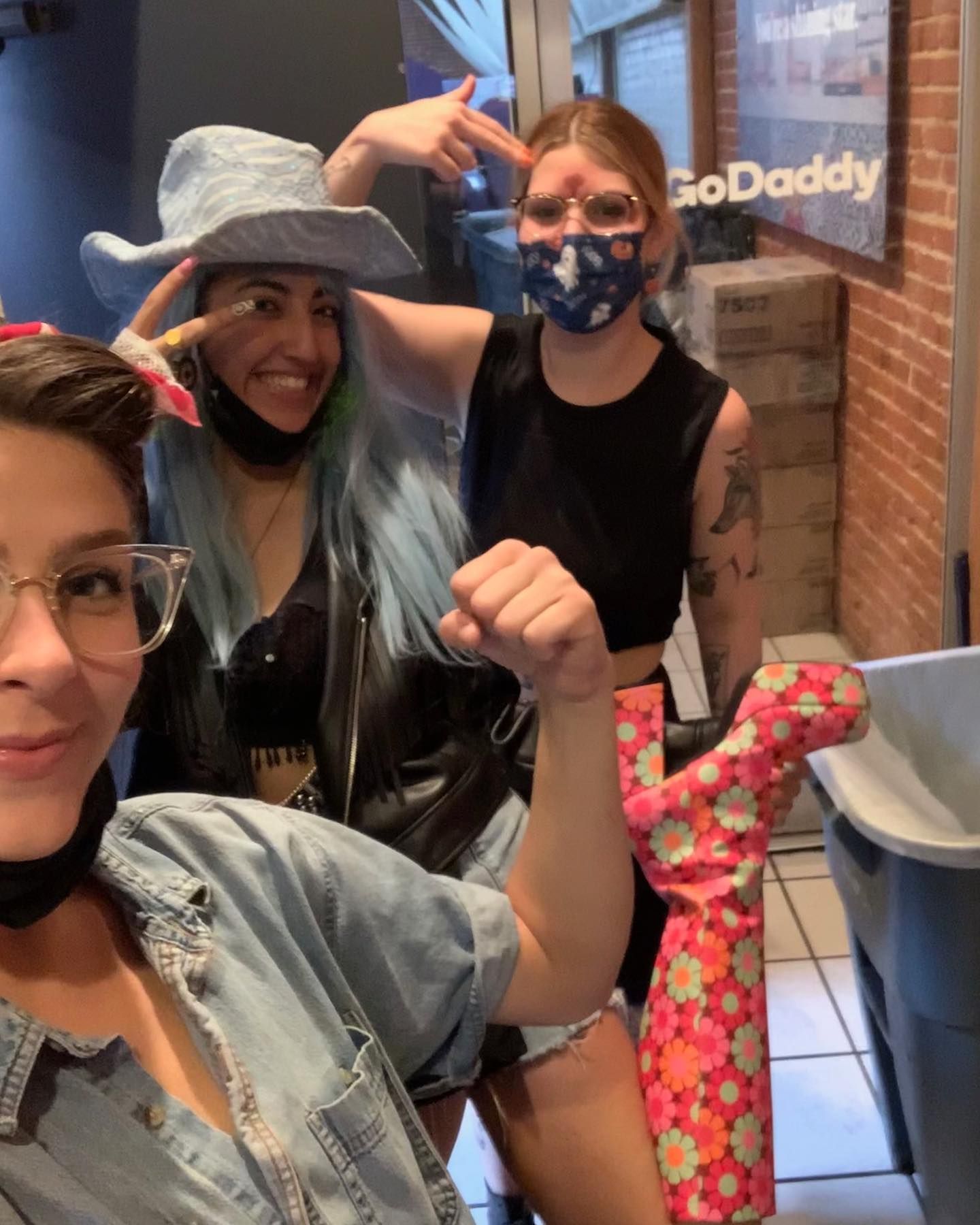 Three women are posing for a picture in front of a sign that says godaddy