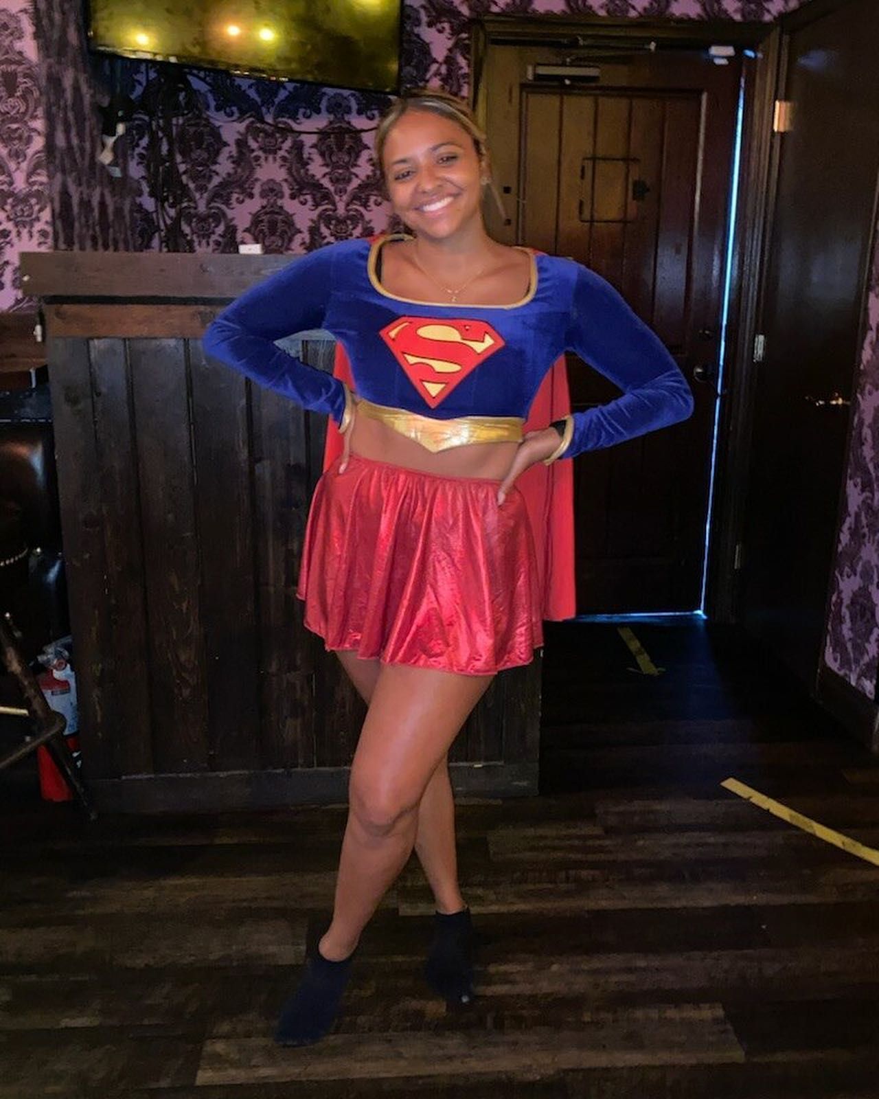 A woman in a superman costume is standing in a room.