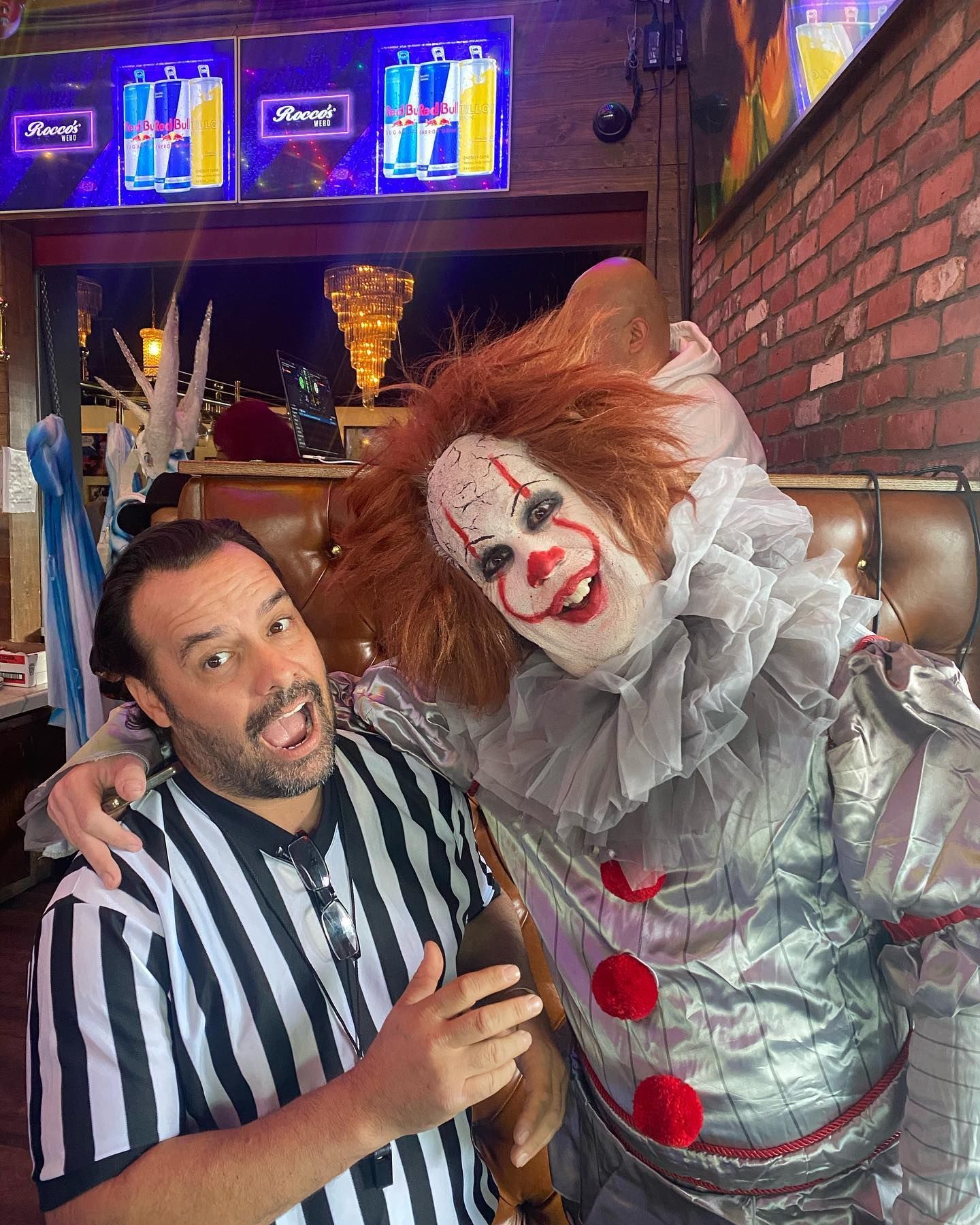 A man in a clown costume is posing for a picture with a referee.