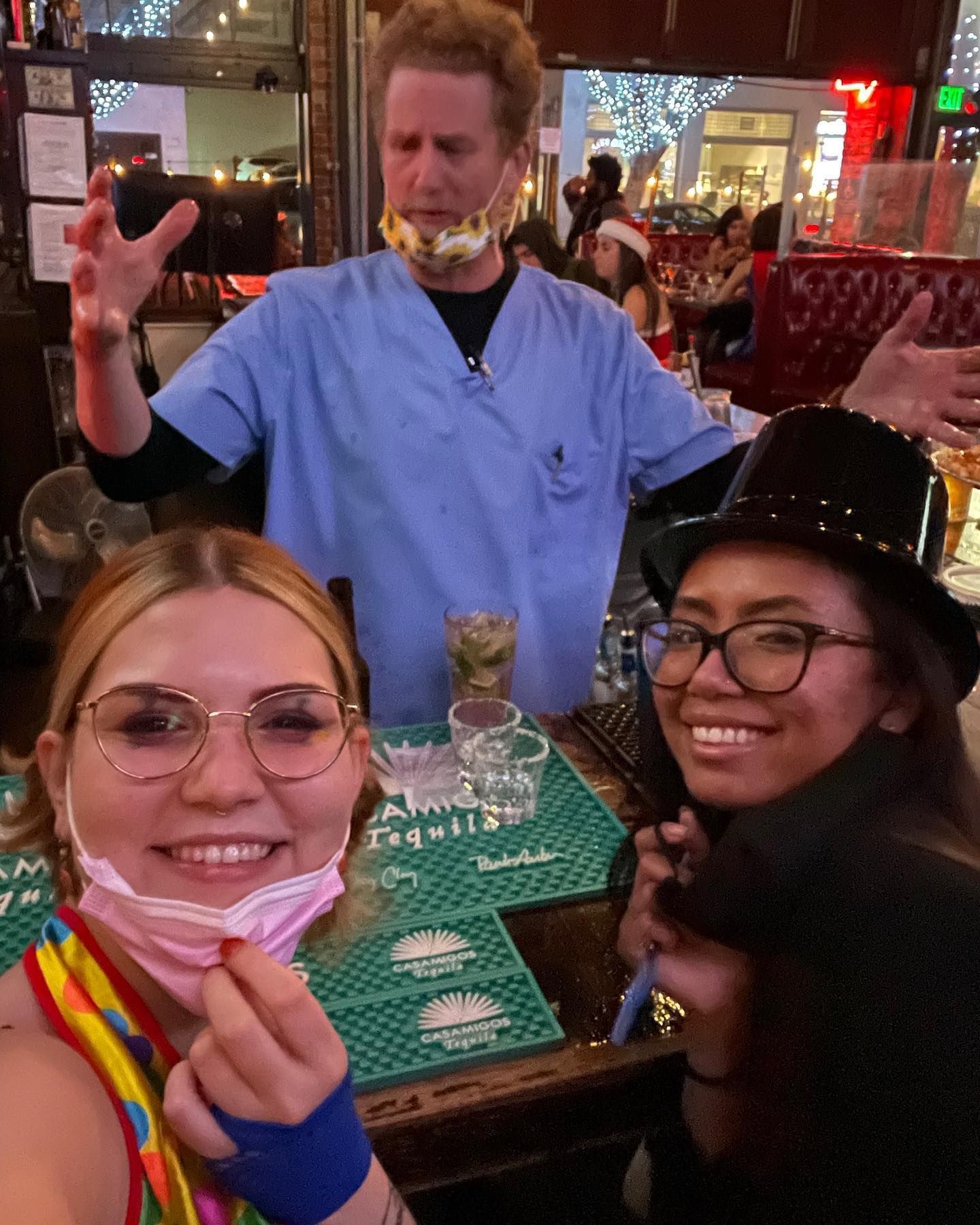 A man in a scrub top is standing behind two women wearing masks